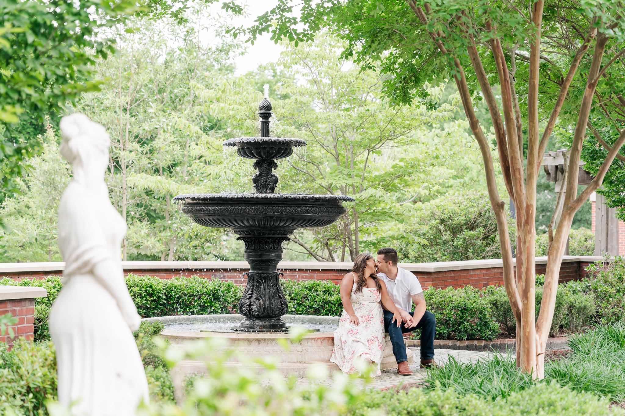 A couple kissing by a fountain in what looks like a secret garden.