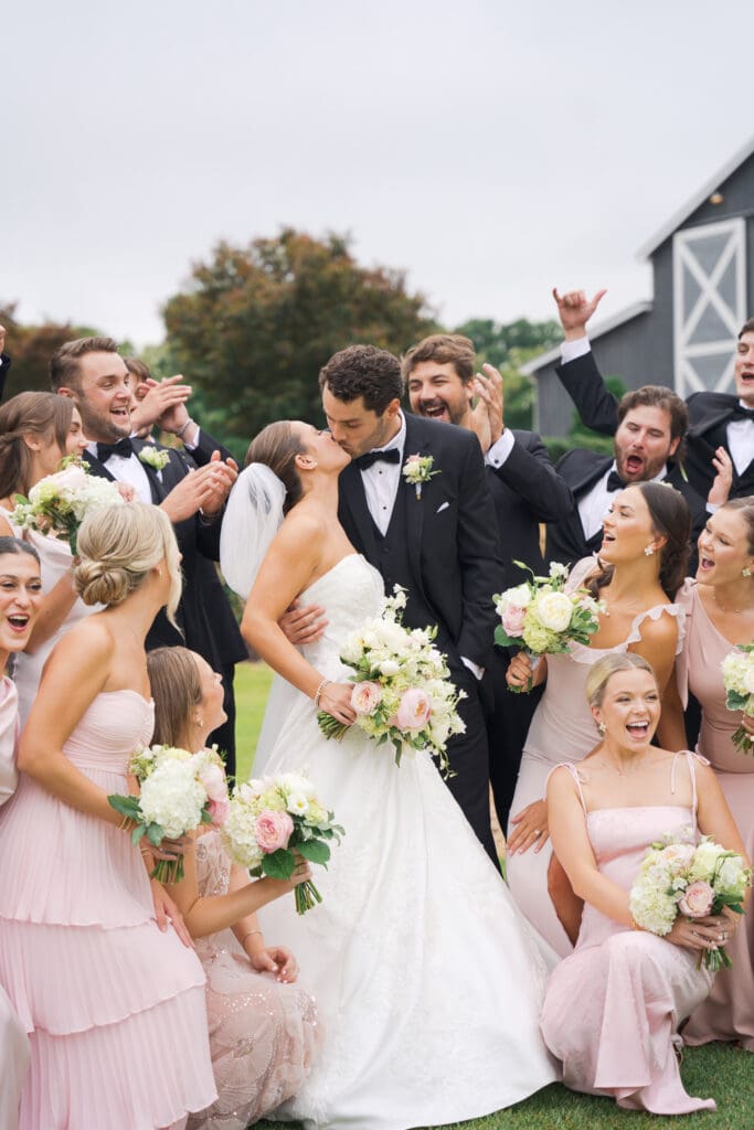 A bride and groom kissing amongst their wedding party