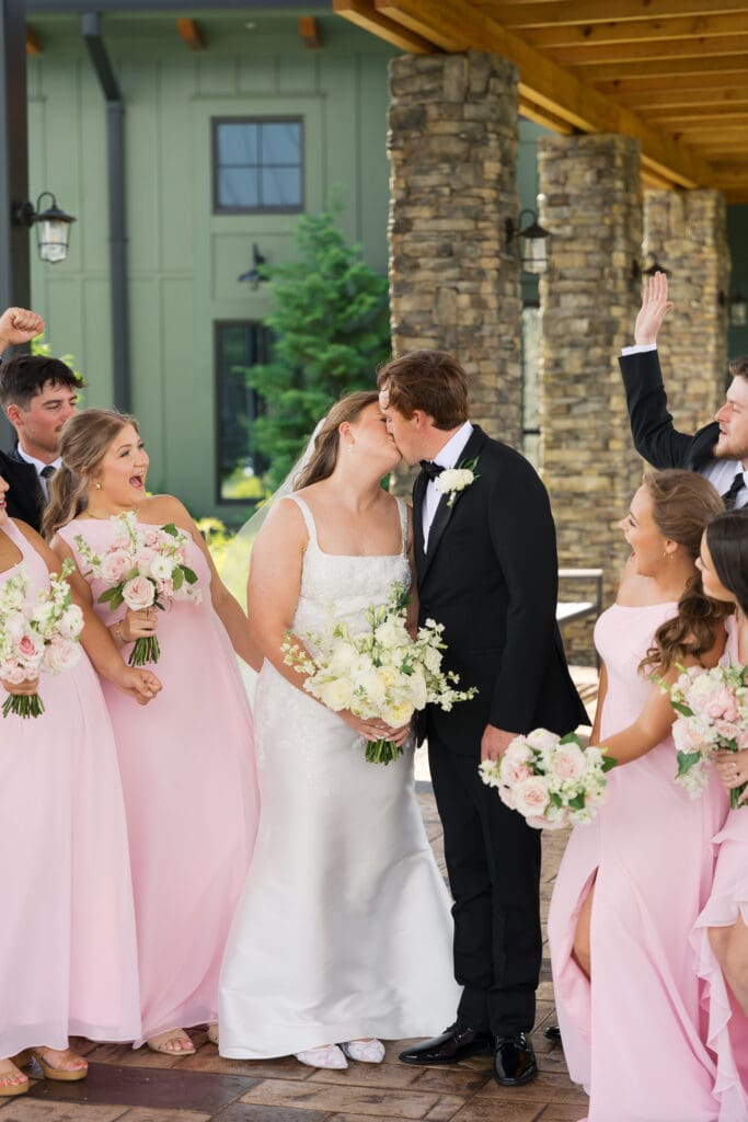 a bride and groom kissing while their bridal party cheers them on