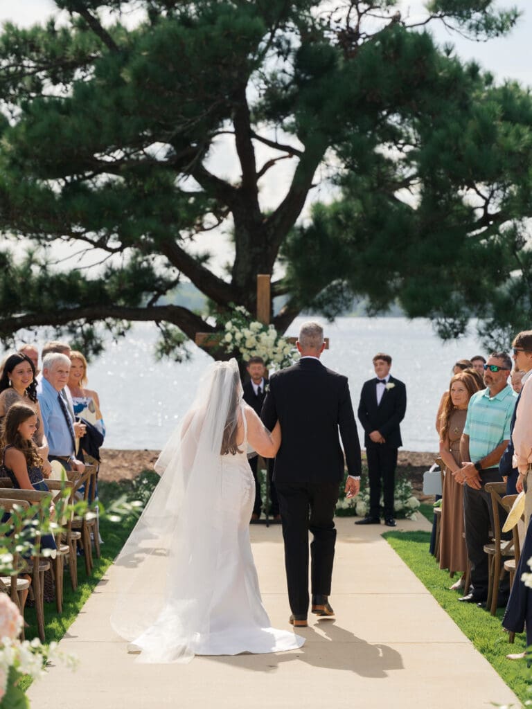 A father walking the bride down the aisle surrounded by their loved ones on a sunny beautiful day