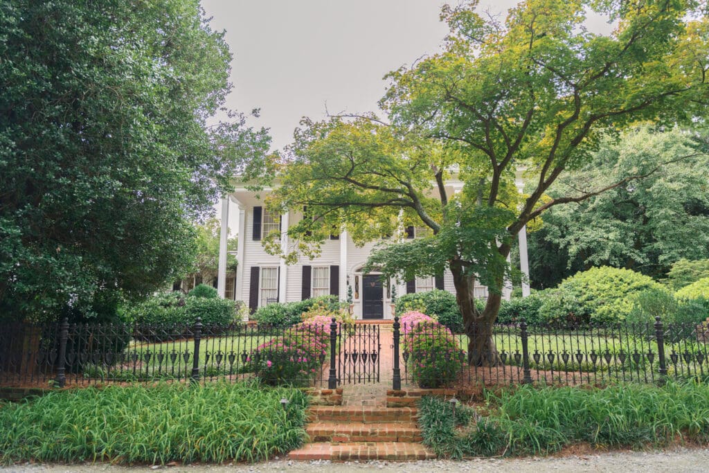 a historic house called flint hill with large trees surrounding the white home that has black shutters
