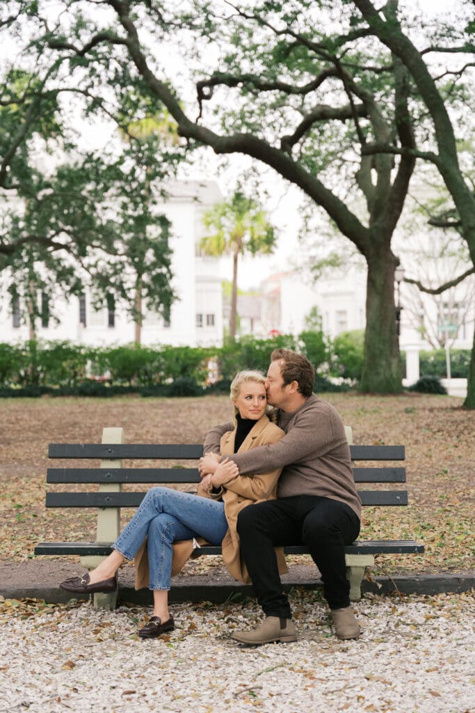 A couple embracing each other sitting on a park bench in downtown Charleston on a cold, windy day.