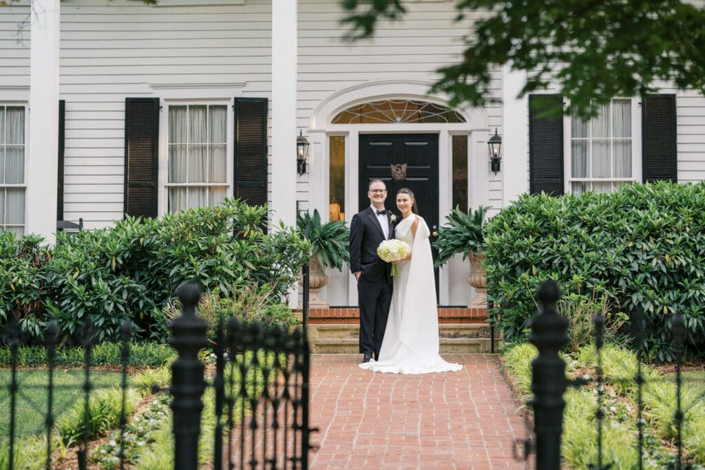 A newlywed couple standing in front of their wedding venue, Flint Hill, surrounded by lush gardens. Photographed by Sara Bartley Photography in Atlanta, Georgia